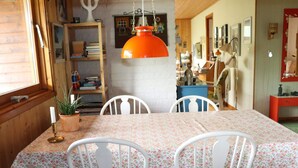 A dining area with a table covered in a floral tablecloth, white chairs, and a hanging orange pendant light.