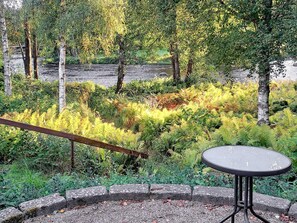 Une table ronde d’extérieur, dotée d’un cadre en métal et entourée d’une bordure en pierre, se dressant sur un fond de verdure luxuriante et d’arbres.