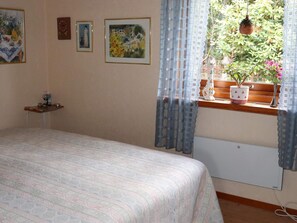 A bedroom with a bed, a window with curtains, a radiator, and a small table with a vase and a clock on the wall. - 5 Star Holiday Home in Knared (Knared)