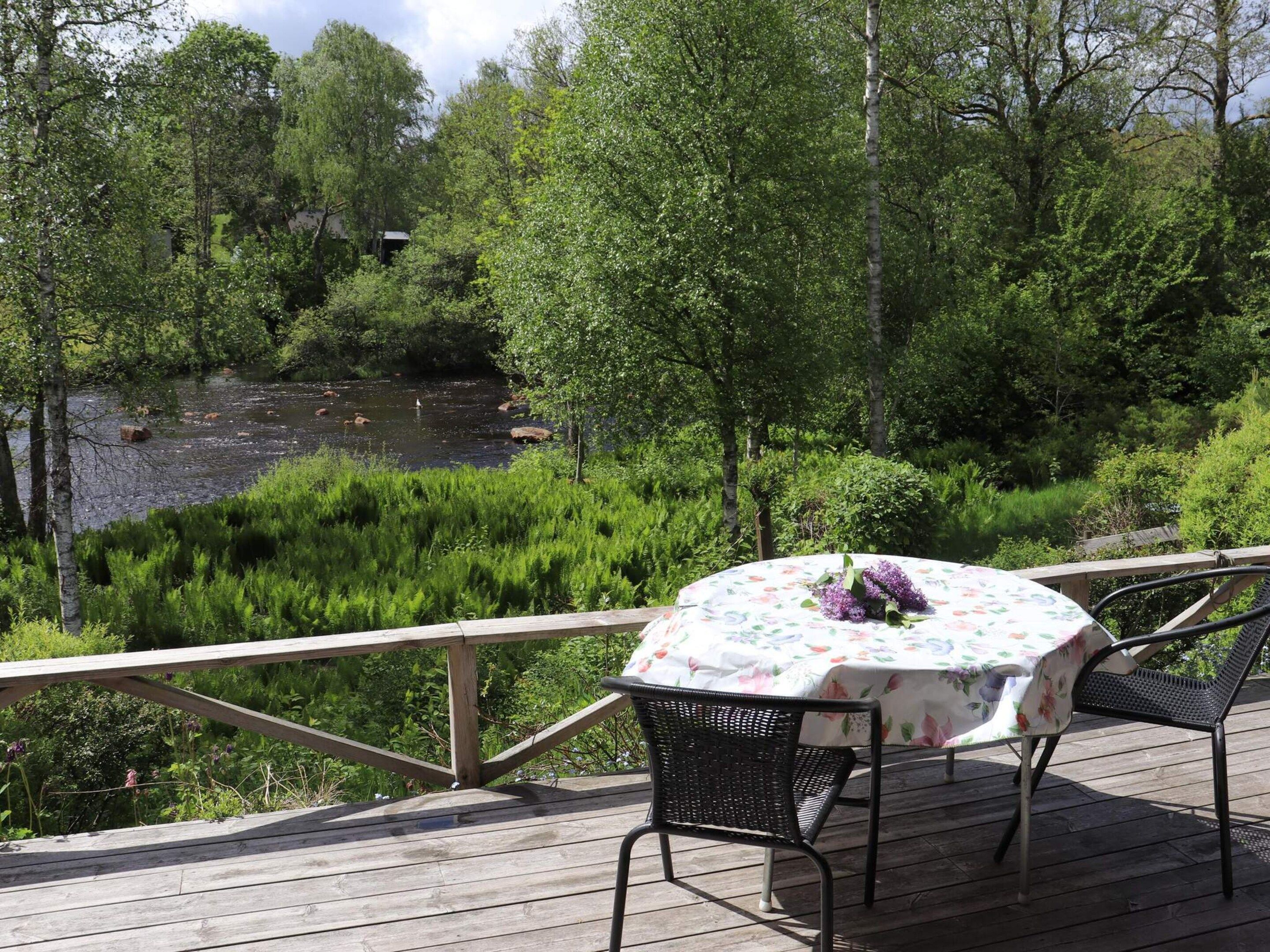 A wooden deck with a table and chairs overlooking a river and forest.