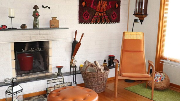 A cozy living room with a fireplace, a comfortable armchair, a wooden bench, and a variety of decorative items.