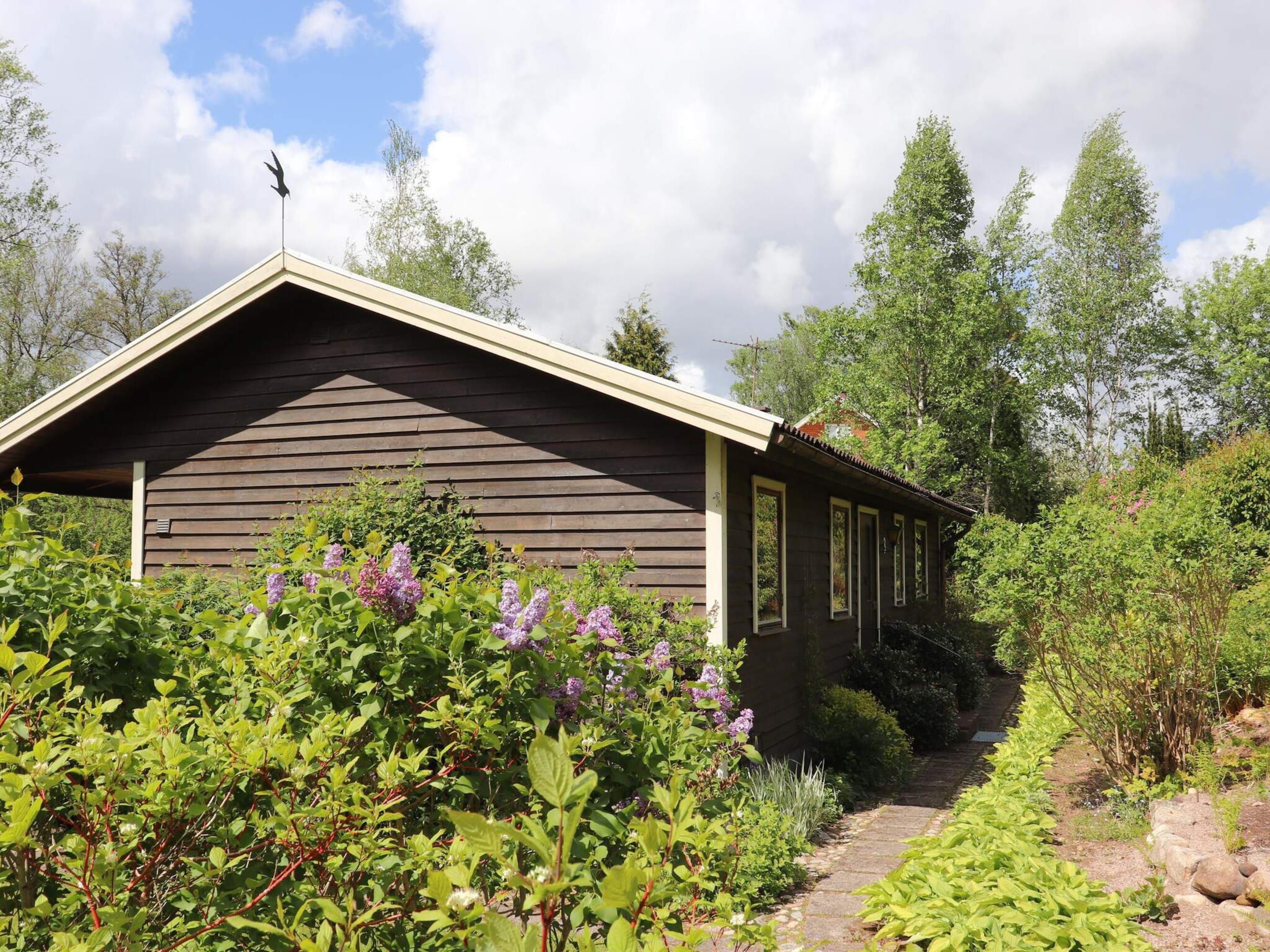 A small cabin with a sloped roof, surrounded by lush greenery and a clear sky.