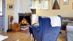 A cozy living room with a fireplace, wooden flooring, a blue armchair, and a sofa. - 7 Person Holiday Home in Tyreso-by Traum (Tyreso)