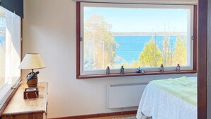 A bedroom with a large window, a bedside table with a lamp, a radiator, and a bed with a green blanket. - 7 Person Holiday Home in Tyreso-by Traum (Tyreso)