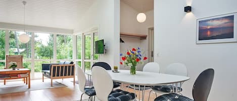 Een moderne eetruimte met een ronde tafel, zes stoelen en een bloemenvaas.