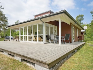 A covered patio with a wooden deck, glass walls, and outdoor furniture. - 6 Person Holiday Home in Aakirkeby (Akirkeby)