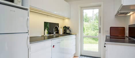 Una cocina moderna con armarios blancos, un microondas integrado y una cafetera.