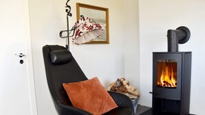 Ein modernes Wohnzimmer mit einem schwarzen Ledersessel, einem schwarzen Kaminofen und einem gerahmten Bild an der Wand.