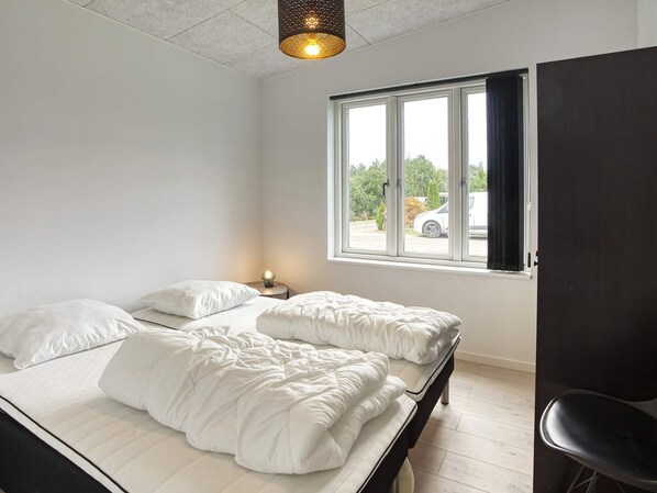 A bedroom with a bed, a nightstand, a lamp, a window, and a view of the outside. - 5 Star Holiday Home in Vaeggerlose (Vaeggerlose)