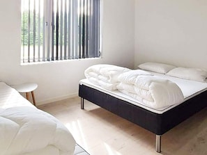 A bedroom with a bed, a bedside table, and a window with blinds. - 5 Star Holiday Home in Vaeggerlose (Vaeggerlose)