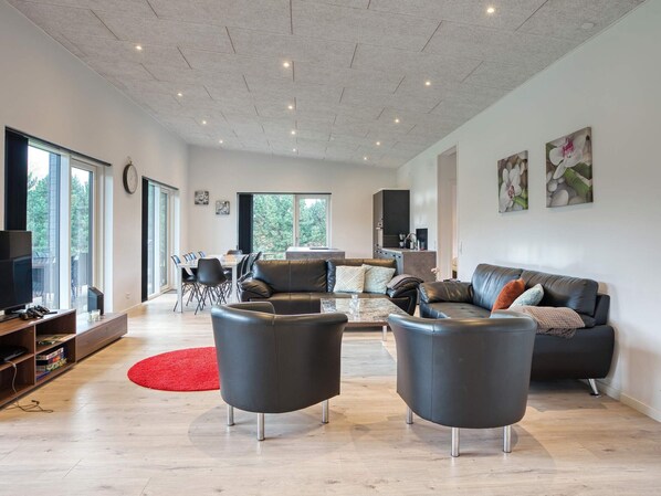 A spacious living area with a modern design, featuring a leather sofa, a dining table, and a kitchen in the background. - 5 Star Holiday Home in Vaeggerlose (Vaeggerlose)