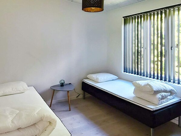 Un dormitorio minimalista con una cama, una mesita pequeña y un ventanal con persianas verticales.