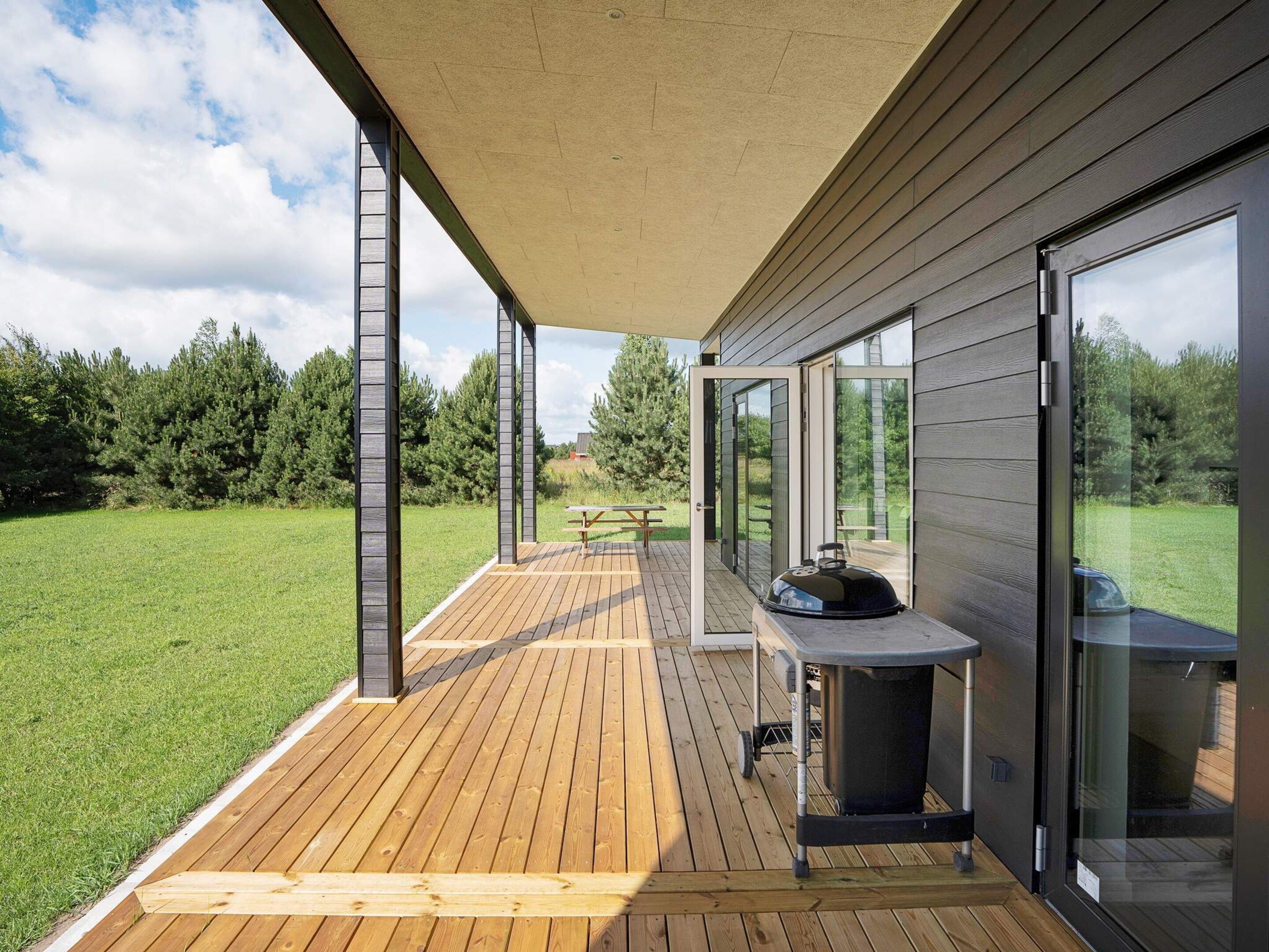A modern outdoor deck with a grill and a picnic table, surrounded by a grassy area and trees.