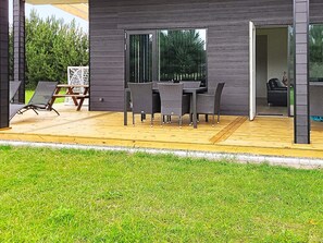A modern outdoor patio with a wooden deck, a dining table with chairs, and a glass door leading to an interior space. - 5 Star Holiday Home in Vaeggerlose (Vaeggerlose)