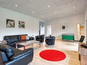 A modern living room with a sofa, chairs, a coffee table, and a dartboard. - 5 Star Holiday Home in Vaeggerlose (Vaeggerlose)