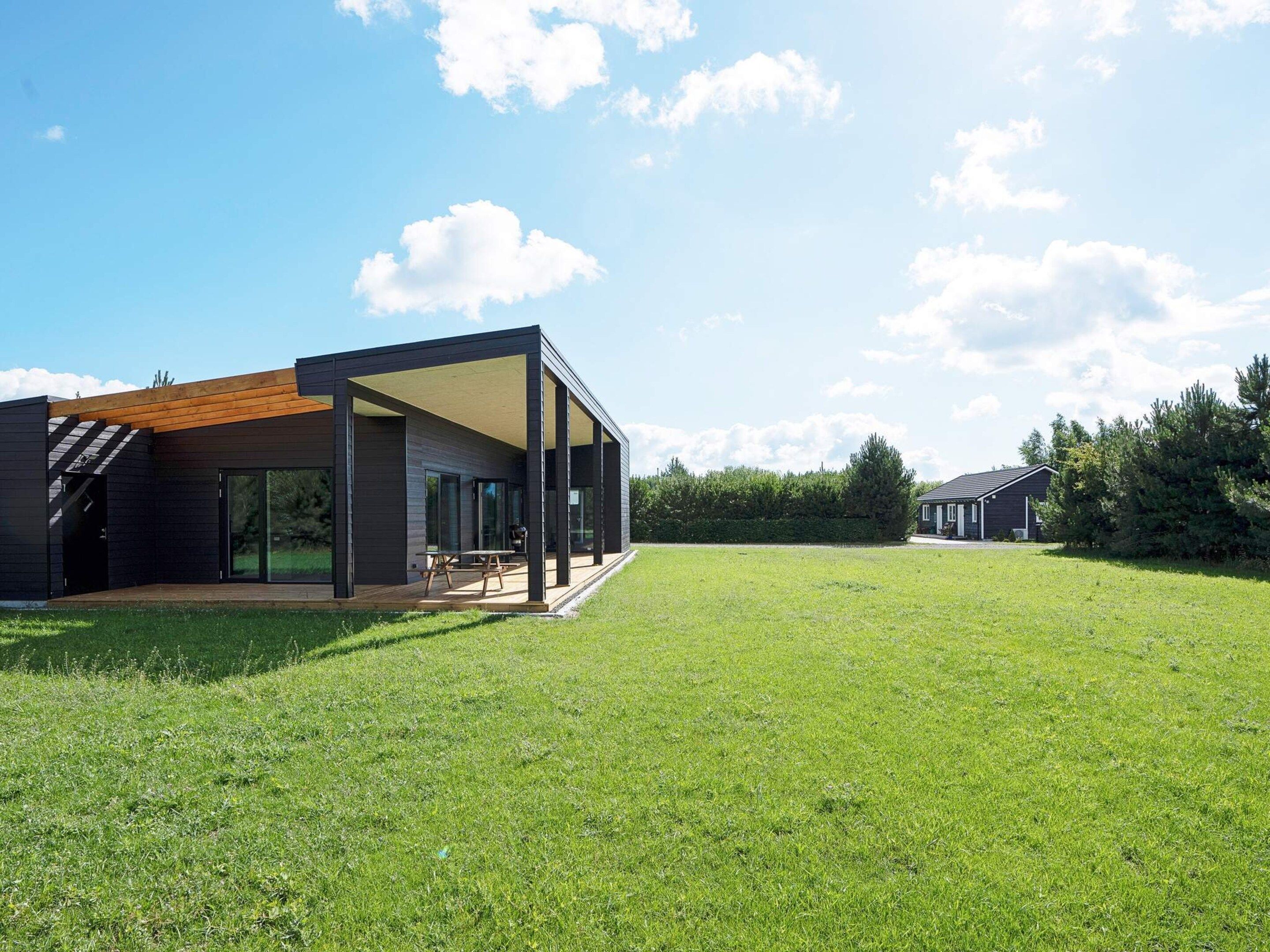 A modern house with a covered patio, a grassy yard, and a neighboring building.