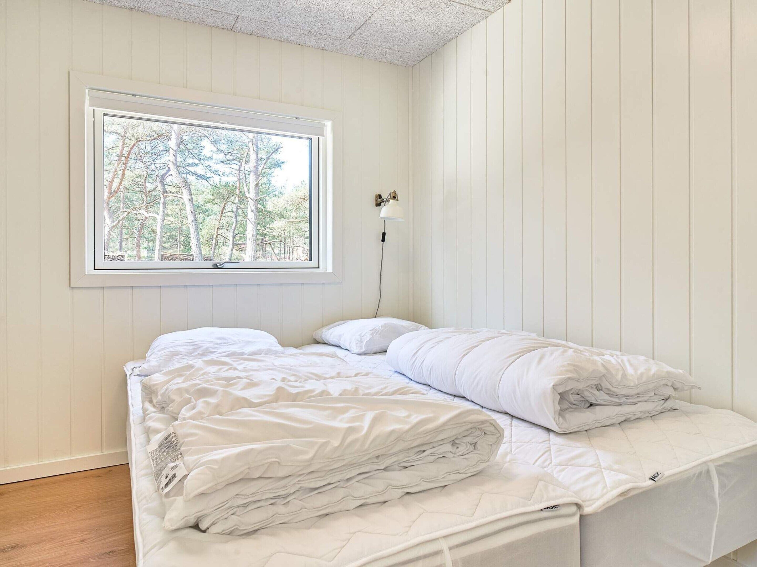 A bedroom with a bed, a window with a view of trees, and a wall-mounted lamp.