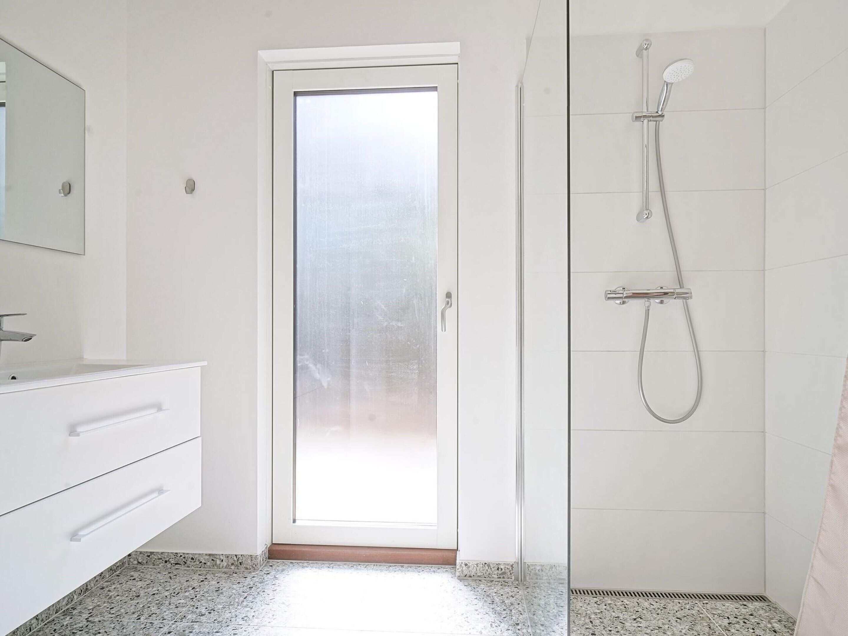 A bathroom with a white vanity, a glass shower enclosure, and a tiled floor.