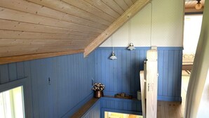 Une pièce avec des poutres apparentes en bois au plafond, des murs lambrissés bleus, une petite fenêtre et un banc en bois.