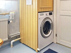 A laundry room with a front-loading washing machine, wooden cabinets, a radiator, and a towel hanging on a rack. - 6 Person Holiday Home in Grastorp (Grastorp)