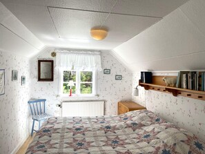 A bedroom with a bed, a chair, a window with curtains, a radiator, and a shelf with books. - 6 Person Holiday Home in Grastorp (Grastorp)
