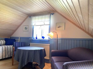 A cozy attic room with a sloped ceiling, a bed with striped bedding, a patterned table, and a patterned sofa. - 6 Person Holiday Home in Grastorp (Grastorp)