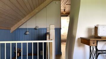 A room with a sloped ceiling, a blue and white wall, a white railing, a sewing machine, and a bed with a floral arrangement.