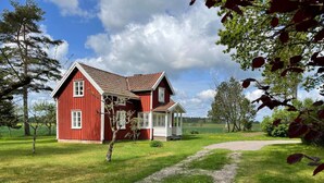 Een rode houten woning met een grindpad en een witte veranda.