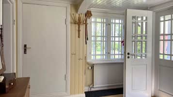 A room with a wooden floor, a white door, a window with a view of greenery, and a radiator.