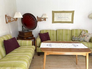 A room with a vintage gramophone, a green-striped sofa, a wooden table, and a framed picture on the wall. - 6 Person Holiday Home in Grastorp (Grastorp)