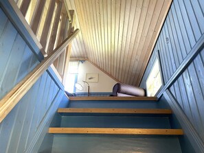 Un escalier avec des marches et des rampes en bois, menant à un palier agrémenté d’un coussin à motifs.