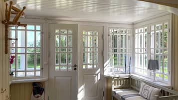 A room with a white door, a bench with a cushion, and a window with a view of greenery.