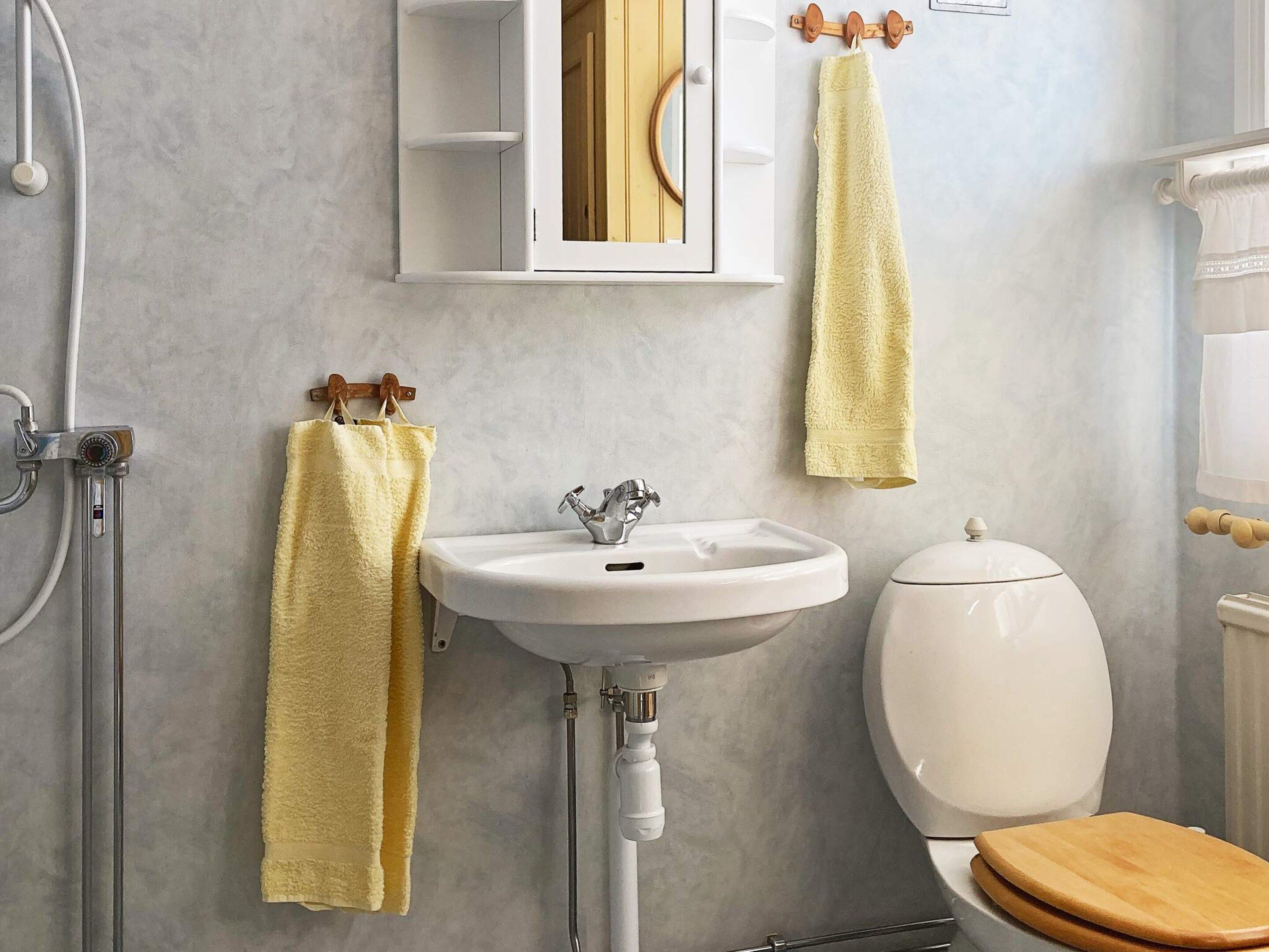 A bathroom with a white sink, a toilet, and a shower. There are yellow towels hanging on hooks.