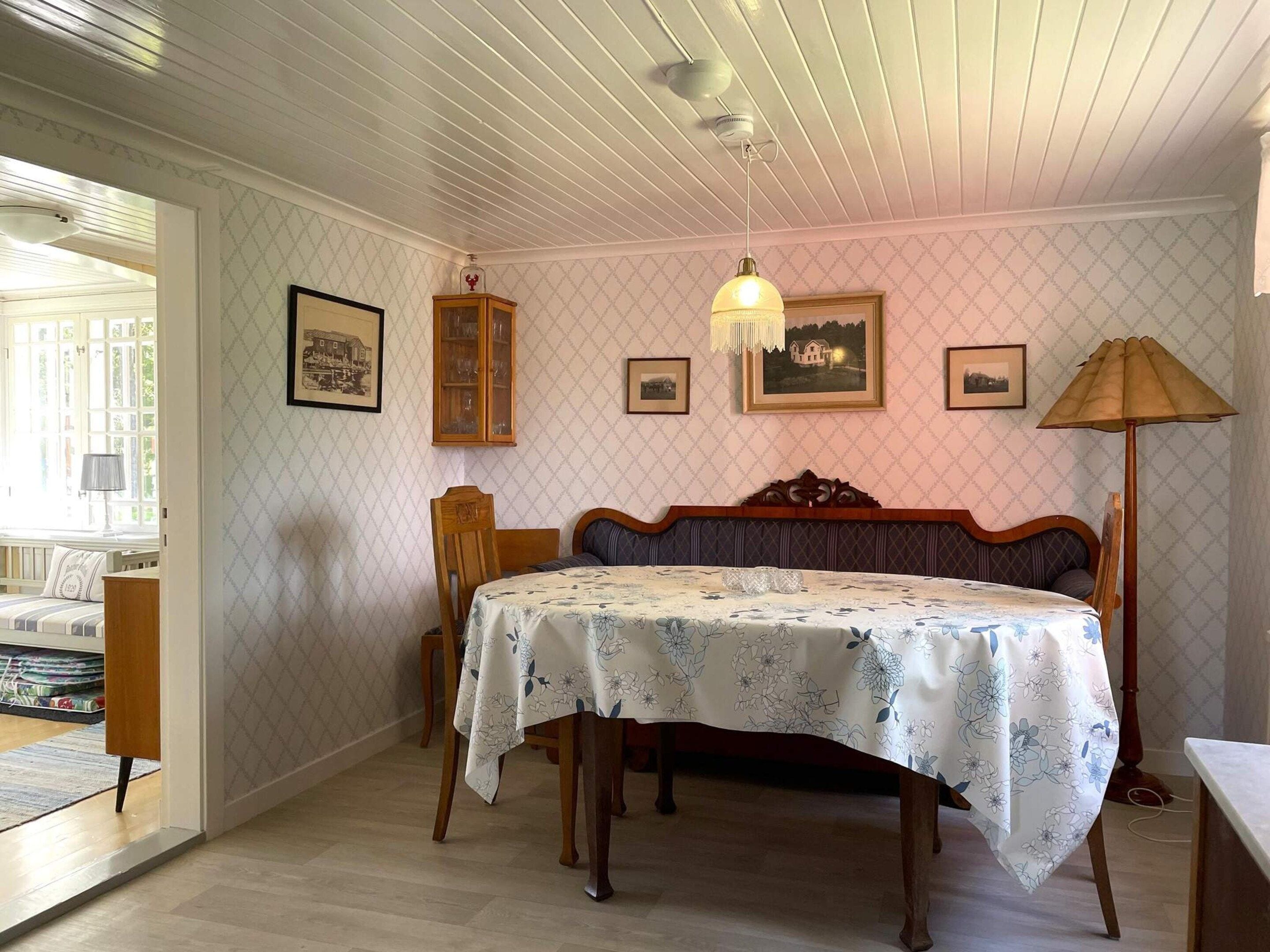 A bedroom with a bed, a wooden headboard, a table with a floral tablecloth, and a lamp.