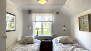 Une chambre avec deux lits simples, une fenêtre avec des rideaux, un bureau et une lampe.