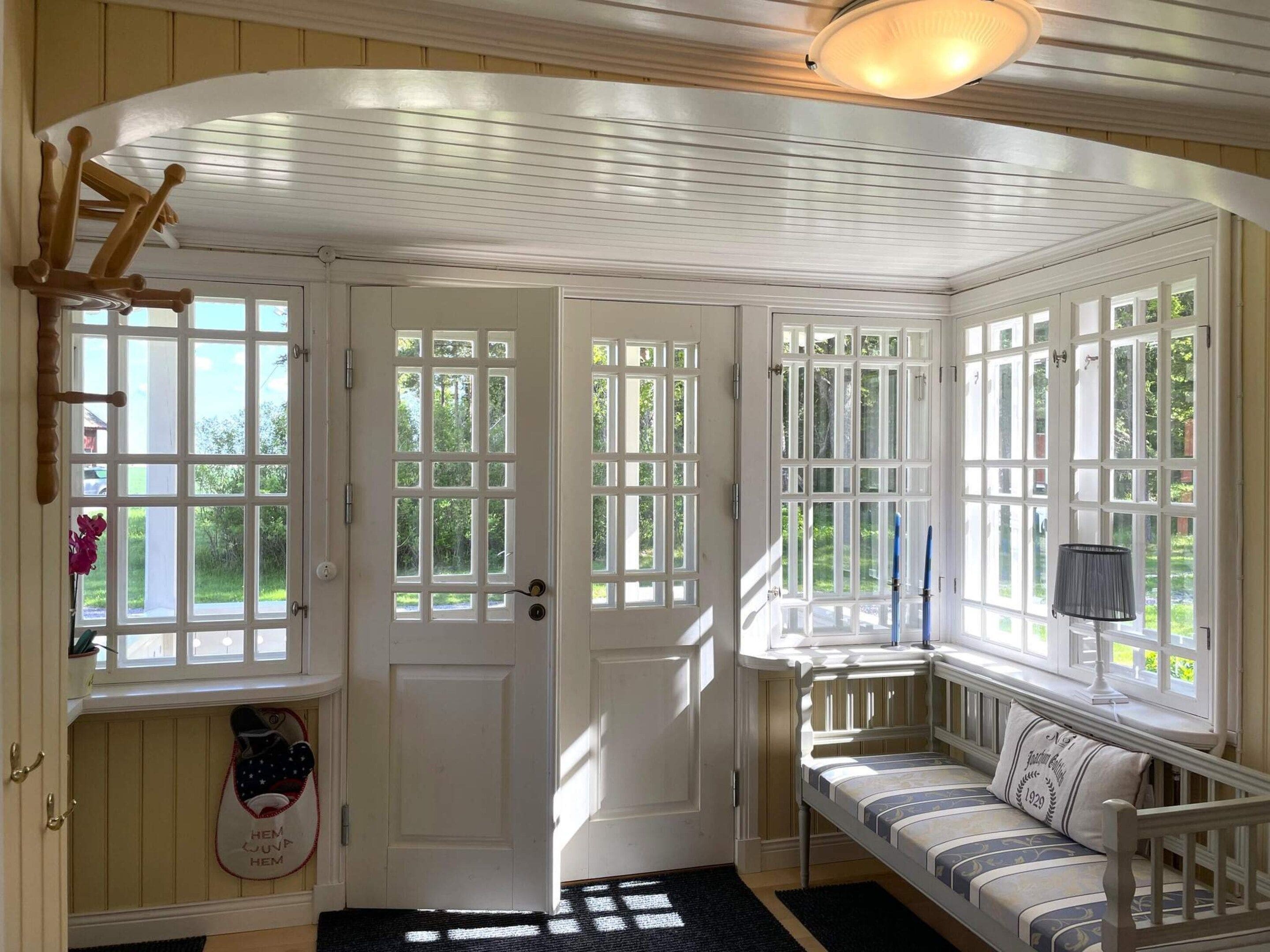 A room with a white door, a bench with a cushion, and a window with a view of greenery.