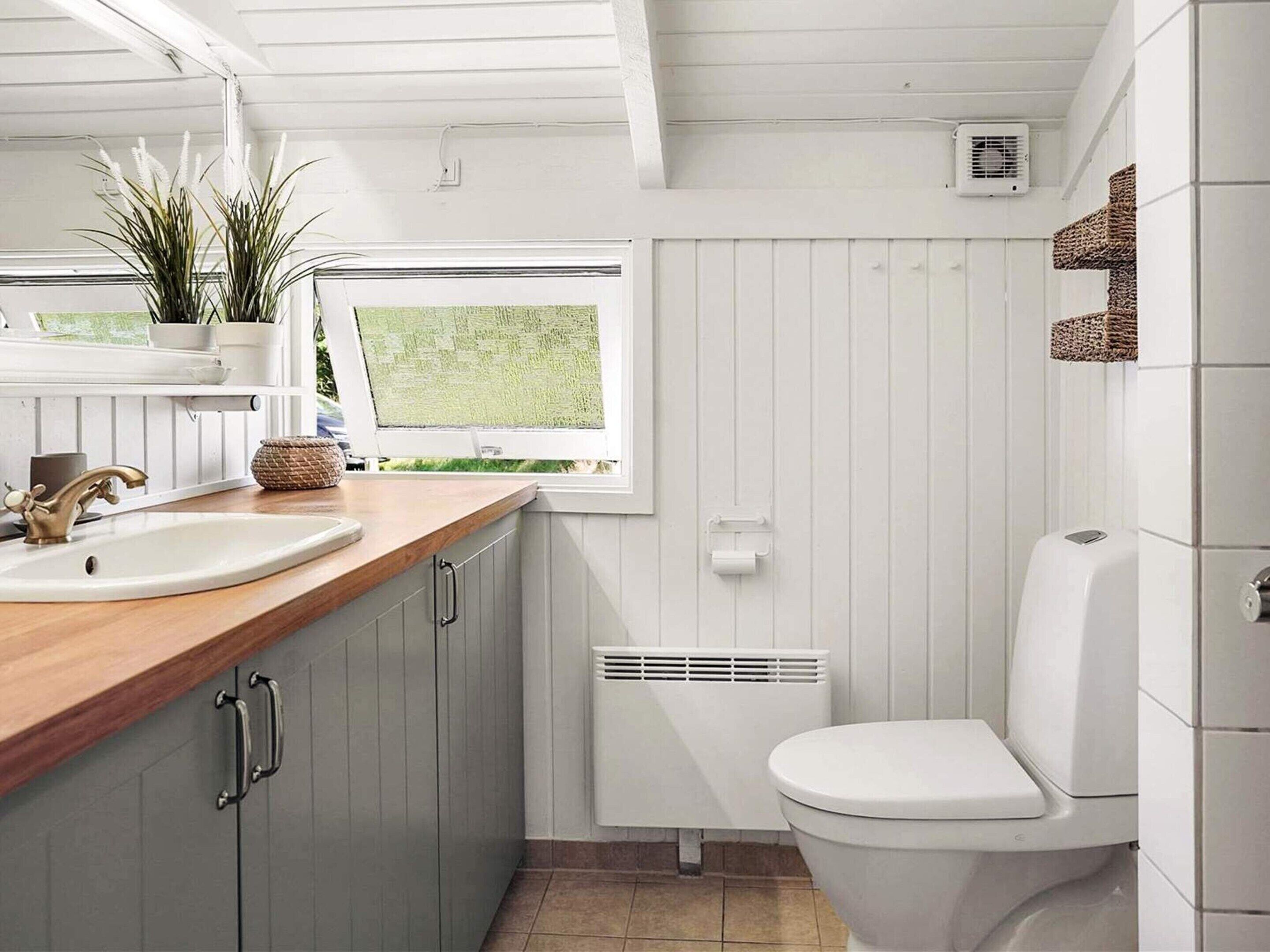 Une petite salle de bain avec un meuble-lavabo en bois, des toilettes blanches et une fenêtre donnant sur un espace verdoyant.