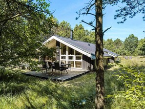 Une cabane dotée d’une terrasse, entourée d’arbres et d’herbe.