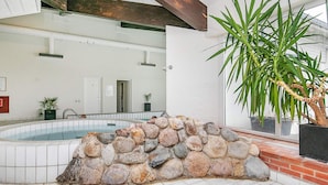 A stone wall surrounding a hot tub in a modern indoor setting with tiled flooring and a large potted plant.