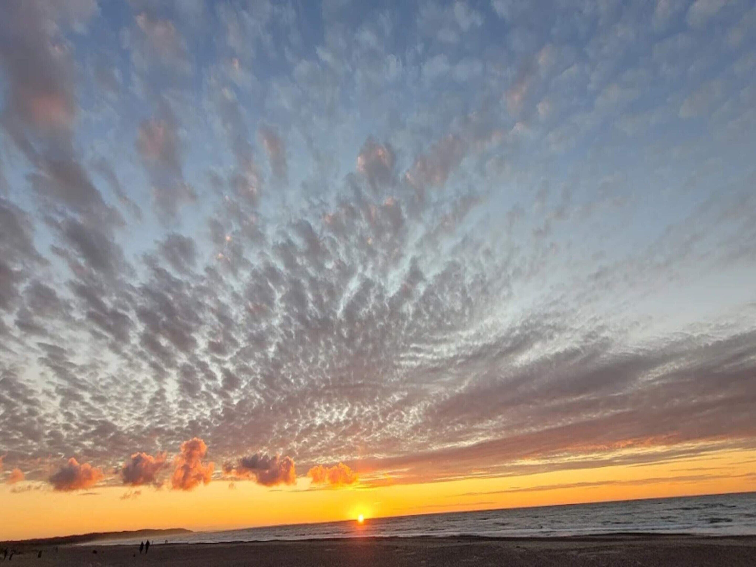 A beach at sunset with a clear sky and the sun setting over the horizon.