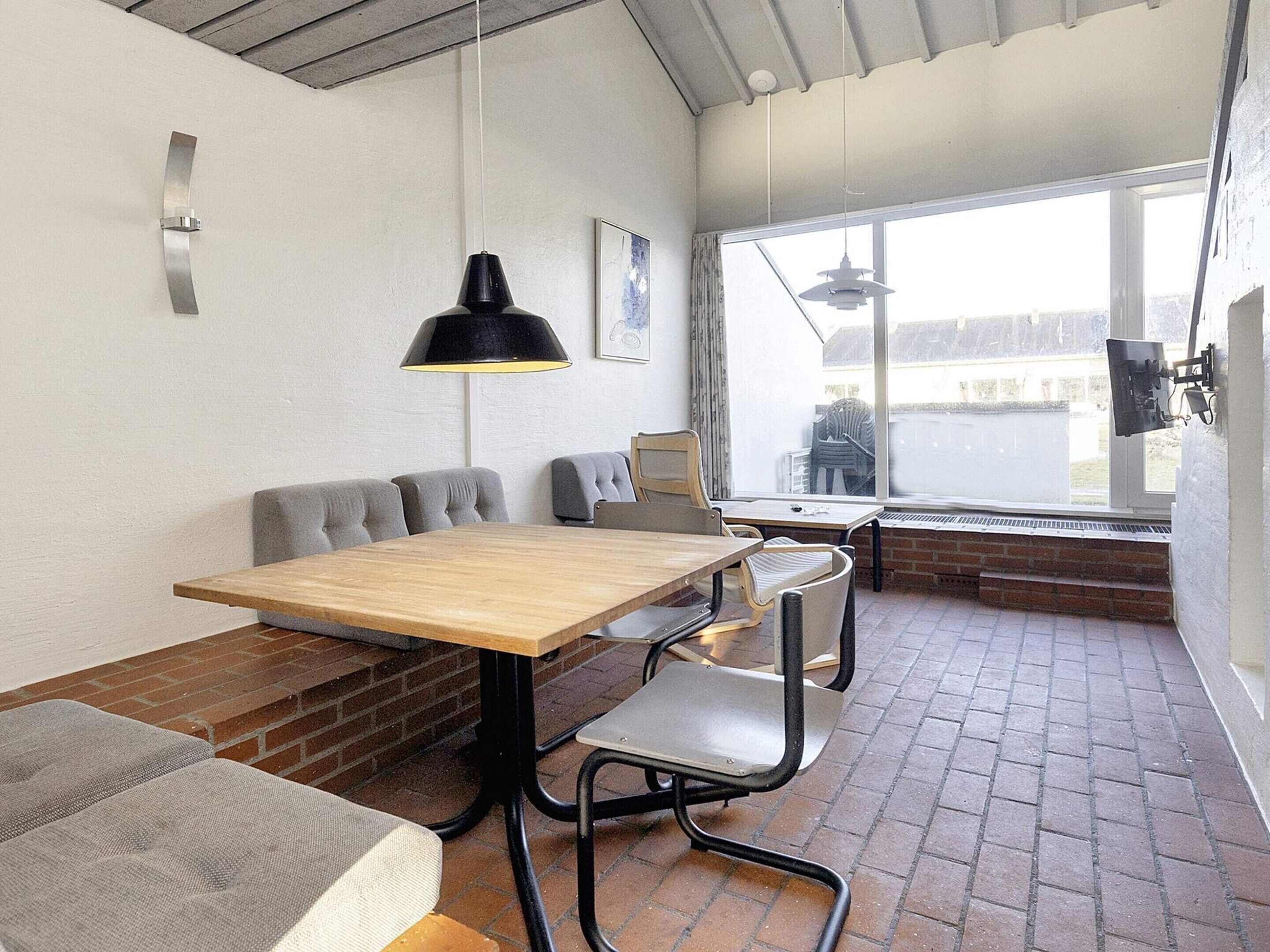 A modern interior with a wooden table, grey upholstered chairs, and a black pendant light.