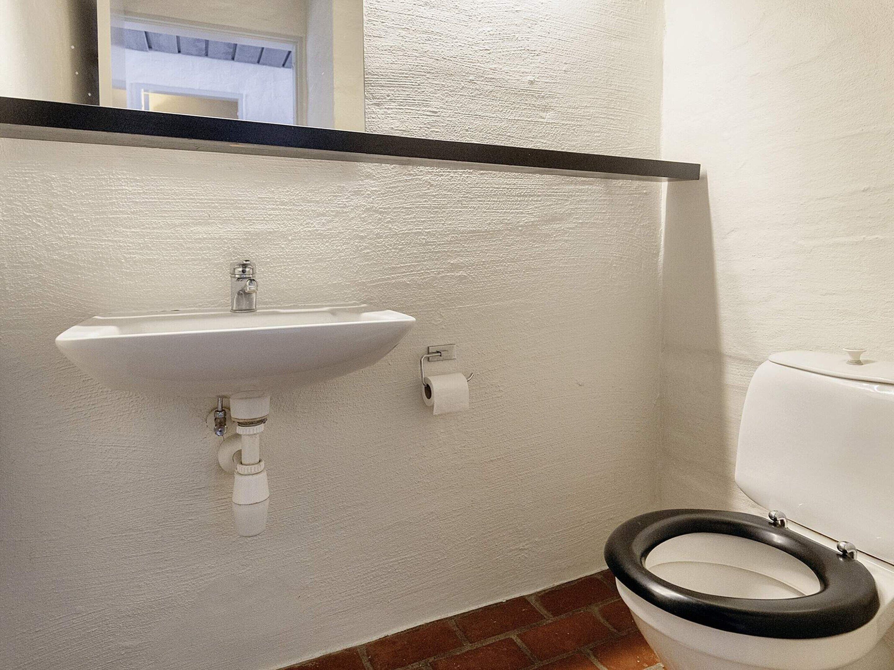 Ein Badezimmer mit einem weißen Waschbecken, einer Toilette und einem sichtbaren Türrahmen.