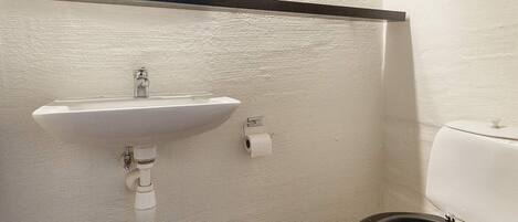 Ein Badezimmer mit einem weißen Waschbecken, einer Toilette und einem sichtbaren Türrahmen.