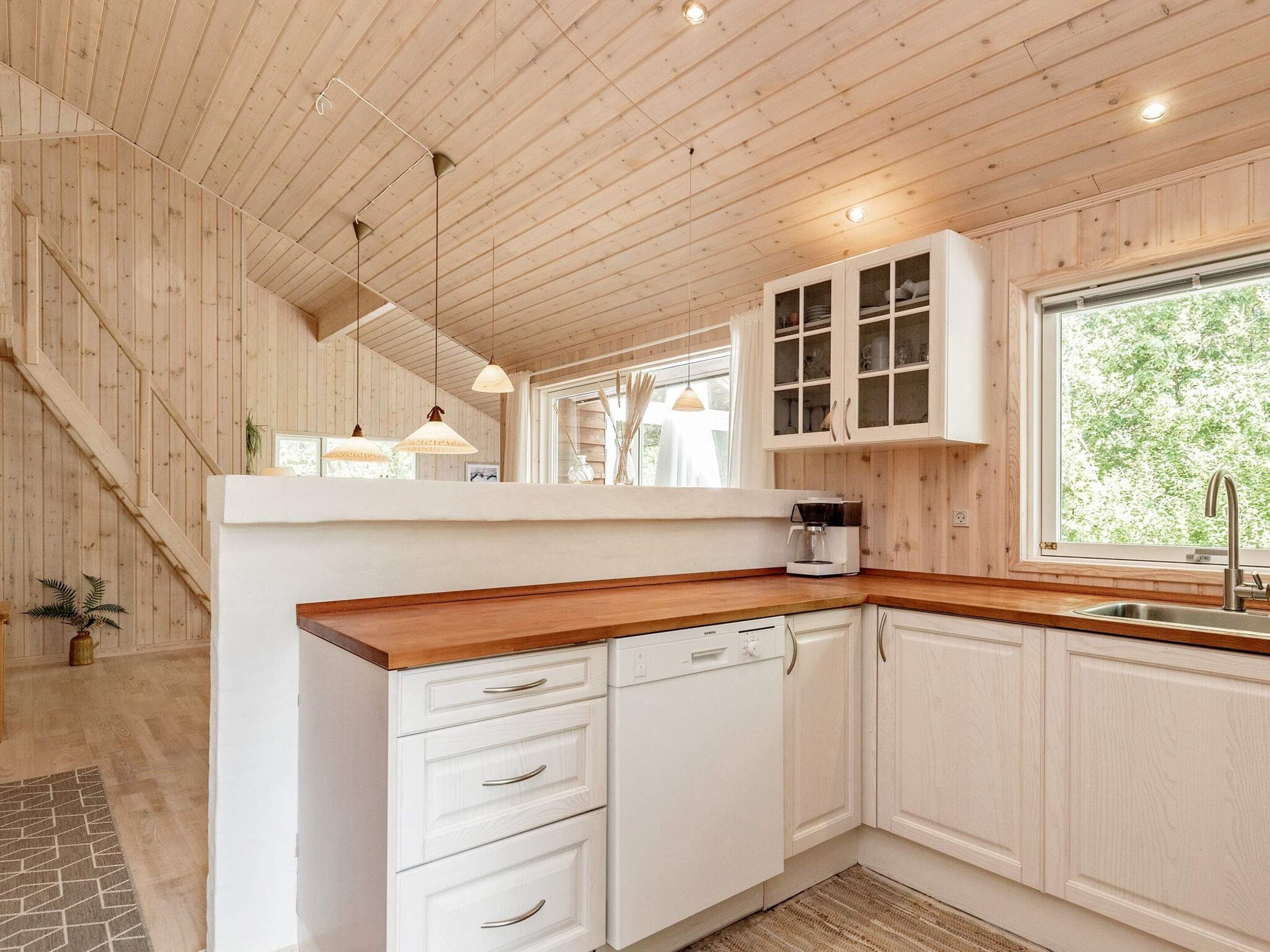A kitchen with wooden ceiling beams, white cabinets, a wooden countertop, and a window with a view of greenery.