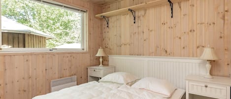 Ett sovrum med träpanel på väggarna, en säng, sängbord och ett fönster.