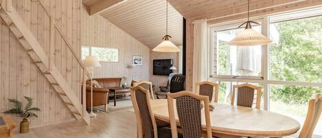 A wooden interior with a dining area, a sofa, and a staircase.