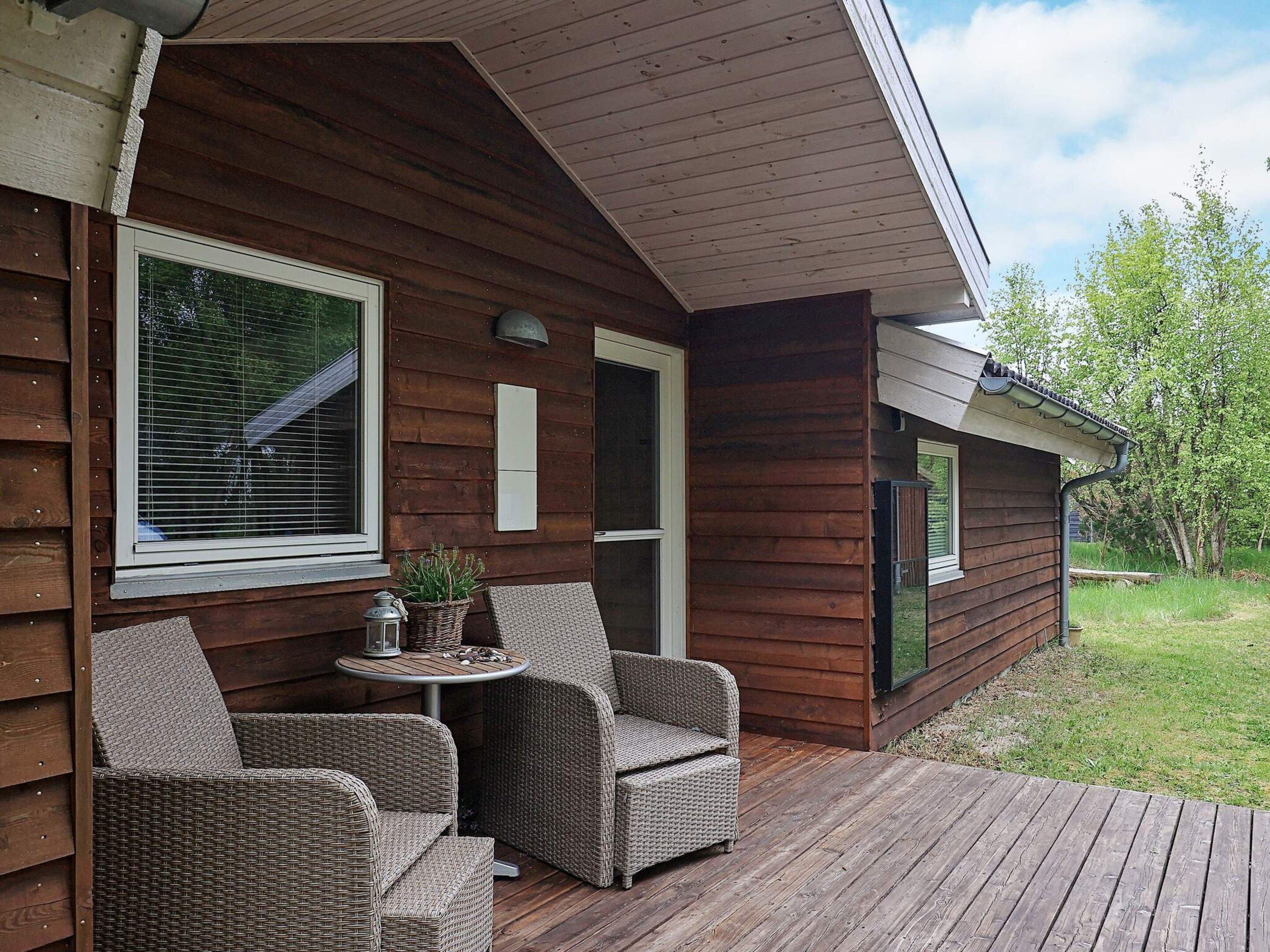 Eine Holzhütte mit einer Terrasse, Korbmöbeln und einem kleinen Tisch mit einer Laterne.