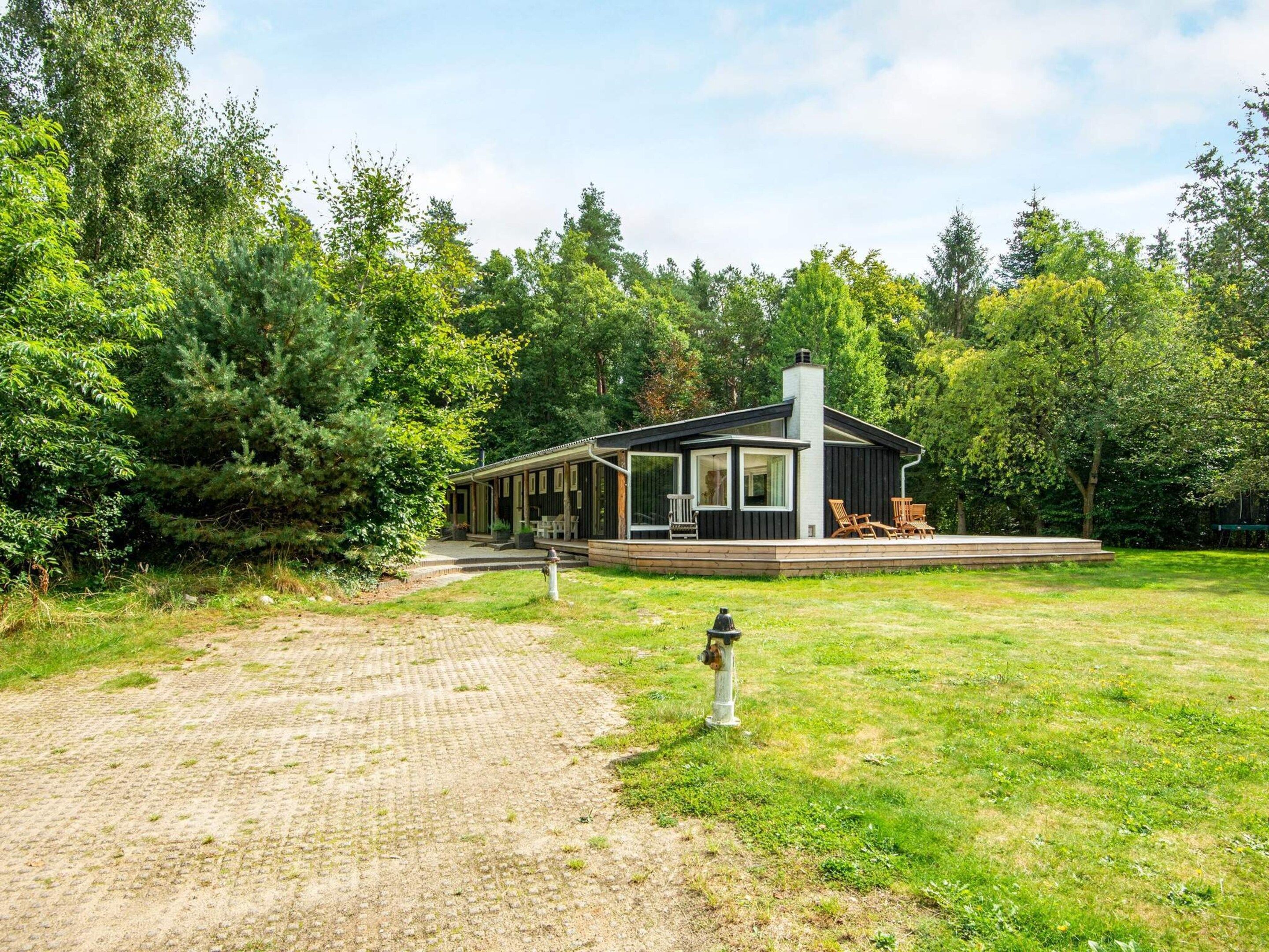 A modern house with a covered porch, surrounded by a grassy yard and dense trees.