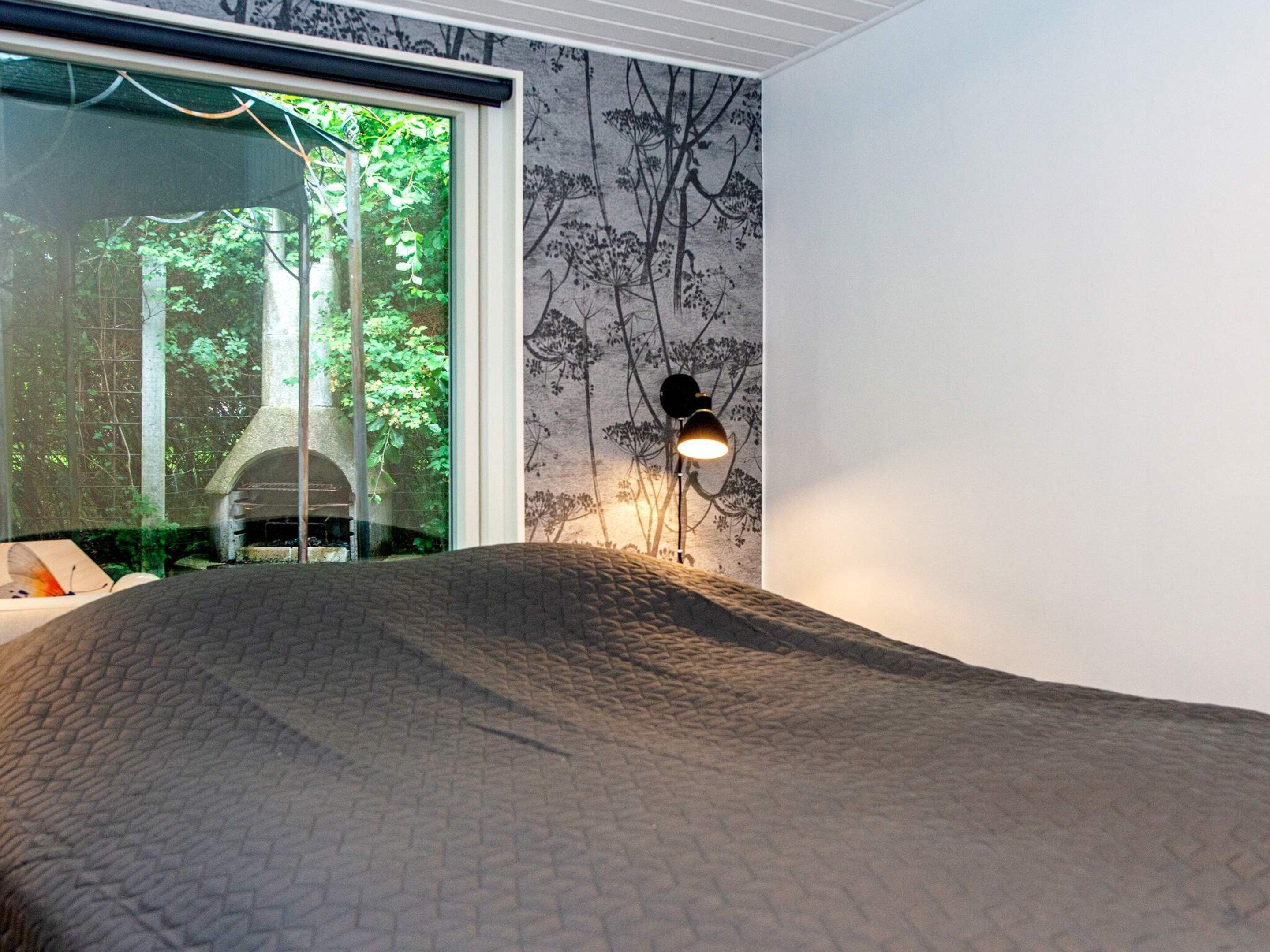 A bedroom with a large bed, a window with a view of trees, and a wall with a tree pattern.