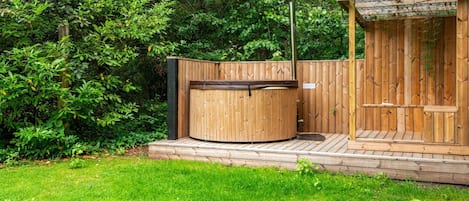 Ein Whirlpool mit Holzterrasse und einem überdachten Holzbau, umgeben von üppiger Vegetation.